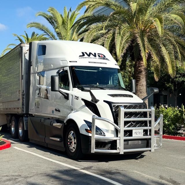 JWD Logistics reefer tractor-trailer parked under palm trees.