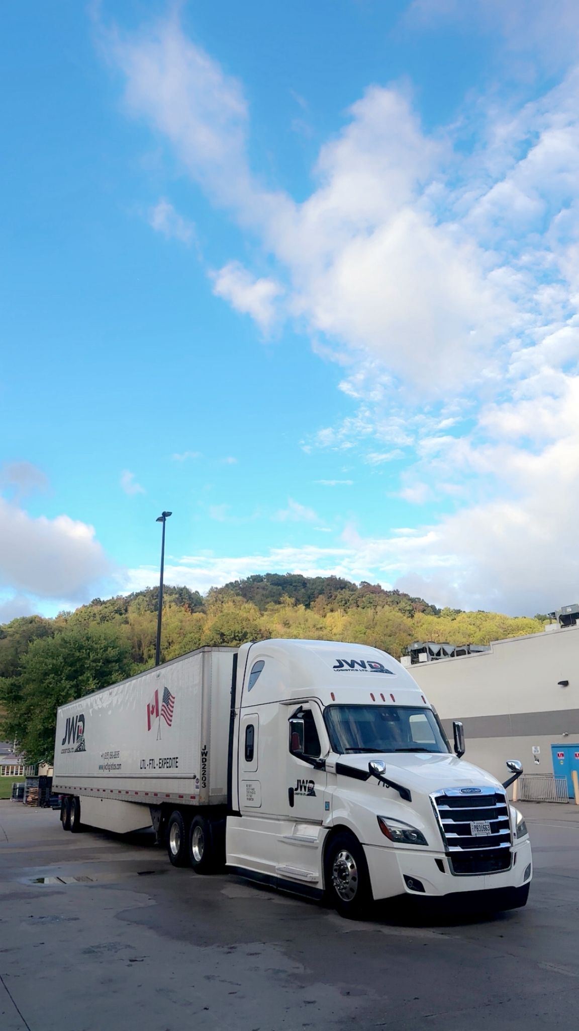 JWD Logistics dry van tractor-trailer parked at the terminal, hills in the background.